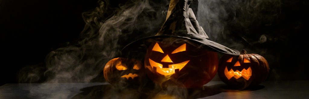 Trois citrouilles-lanternes brillent dans le noir au milieu du brouillard. Citrouille d'Halloween dans un chapeau de sorcière